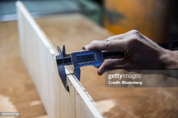 Worker measures the thickness of a length of plyboard using a digital vernier caliper in a workshop at the Eiwlee Industrial Co. Factory in...