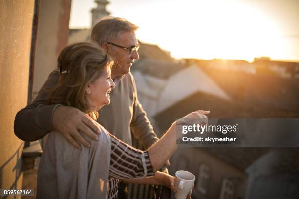 omarmd senior paar genieten in een weergave vanaf hun balkon bij zonsondergang. - conveyor belt point of view stockfoto's en -beelden