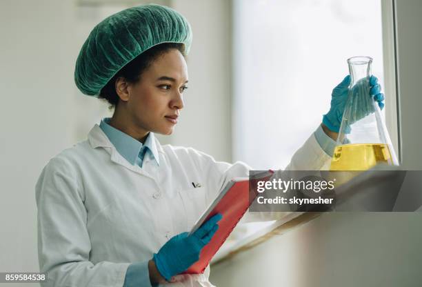 giovane scienziato nero che detiene dati scientifici mentre esamina la sostanza tossica in laboratorio. - cuffia chirurgica foto e immagini stock