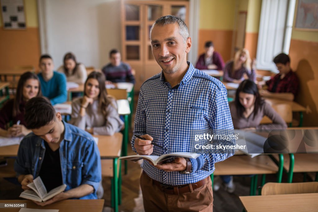 Happy high school teacher looking at camera during the class in the classroom.