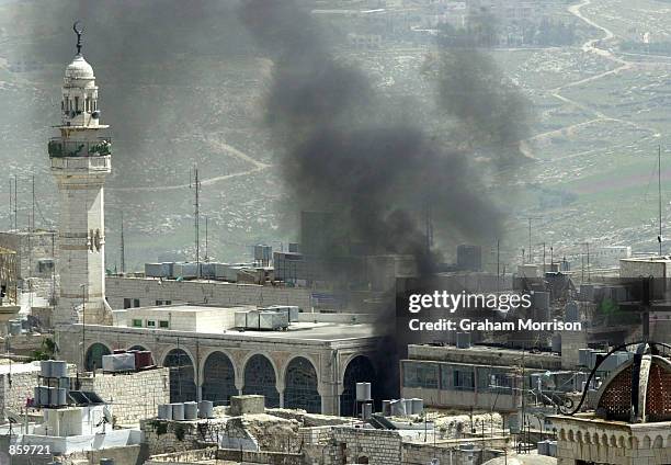 Black smoke rises next to the minaret of the Omar mosque on Manger Square, near the Church of the Nativity compound, April 11, 2002 in the West Bank...