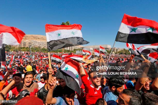 Syrians wave their national flag and cheer on their national team at the Umayyad Square in Damascus as they watch a broadcast of the World Cup...