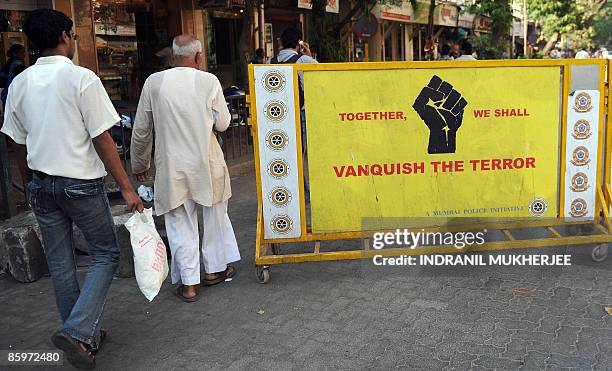 Indian pedestrians walk past a police barricade urging citizens to fight terrorism, close to the Arthur Road jail in Mumbai on April 14, 2009. The...
