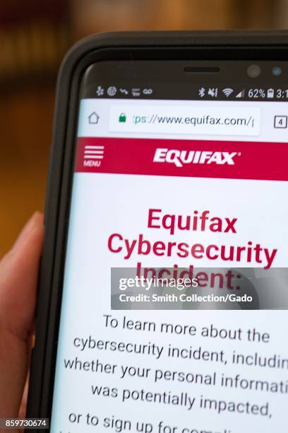 Close-up of a hand holding a cellphone open to the website of credit bureau Equifax, showing information about a 2017 cybersecurity breach in which...