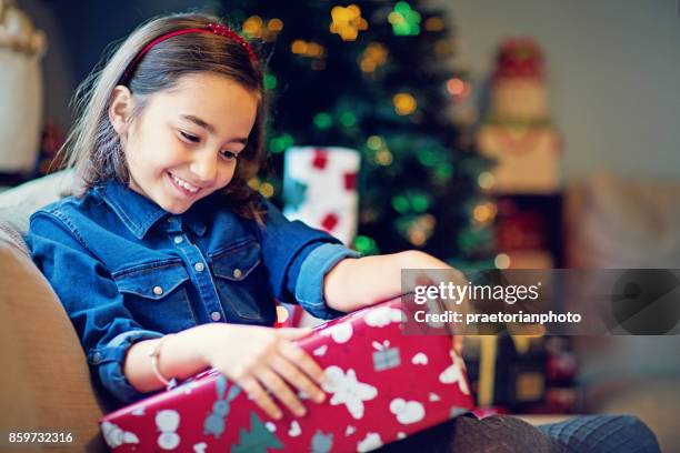 happy girl is opening her christmas gift - christmas morning stock pictures, royalty-free photos & images