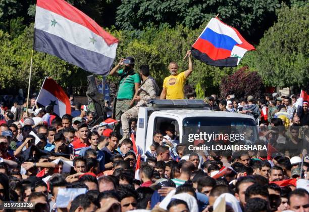 Syrian man waves a Syrian and Russian flag in Umayyad Square in Damascus as fans gathered to watch a live broadcast of the World Cup qualifying...