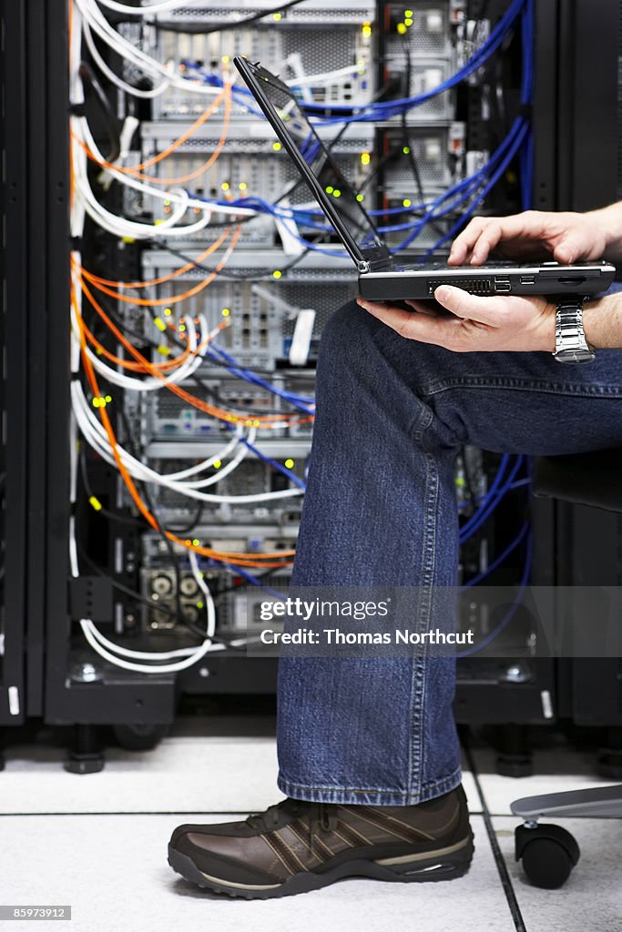 Man using laptop computer, working in server room.