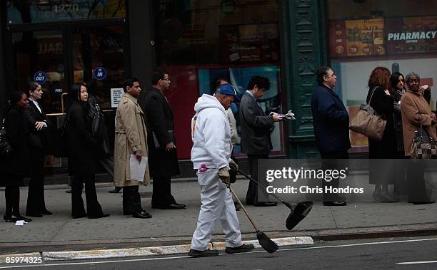 Street sweeper works in front of a line of people waiting to enter a job fair in midtown Manhattan April 14, 2009 in New York City. Job hopefuls...