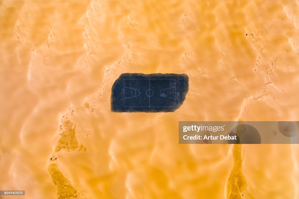 Aerial picture taking with drone of a stunning empty basketball court in the middle of the desert surrounded by dunes in visual and aesthetic picture taken from directly above view.