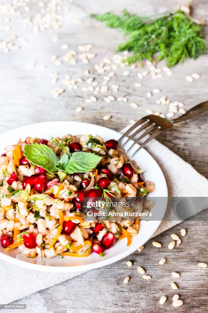 Warm salad with barley, carrot, onion, pomegranate seeds and fresh mint in a plate on a wooden table, selective focus