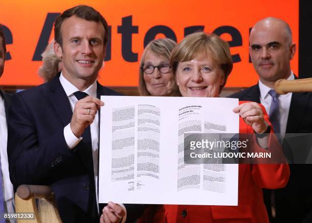 German Chancellor Angela Merkel and French President Emmanuel Macron hold up a print the declaration of Human Rights printed on a replica of the...