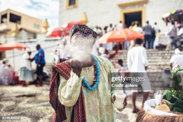 afro-brazilian man in traditional religious costume blowing white powder out of hand - baiano stock pictures, royalty-free photos & images