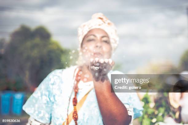 afro-brasilianische frau in religiöser tracht weht weißes pulver aus der hand - traditioneller brauch stock-fotos und bilder