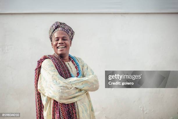 happy afro-brazilian man in traditional religious costume in front of wall - citizenship ceremony stock pictures, royalty-free photos & images