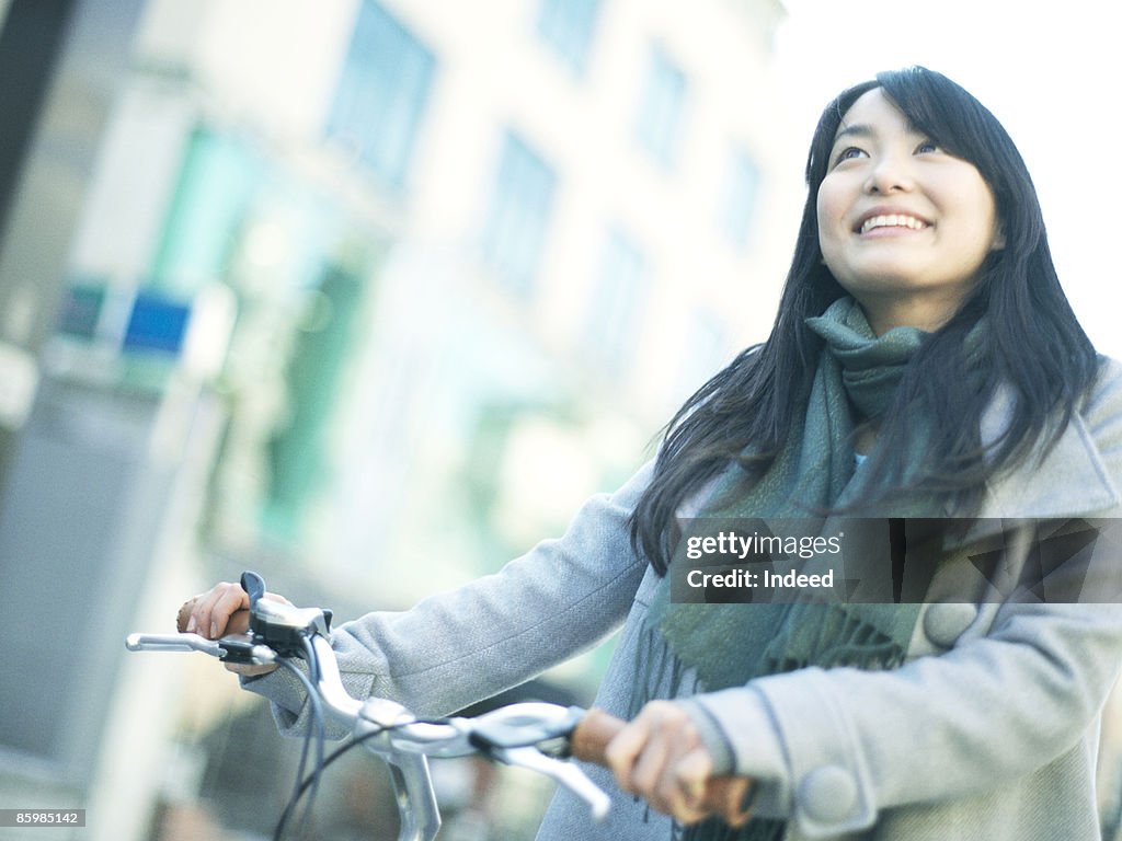 Young woman pushing bicycle and walking, smiling