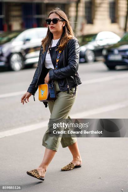 Guest wears sunglasses, a black leather jacket, a white top, a yellow and blue bag, light khaki short pants, leopard print slippers, outside the...