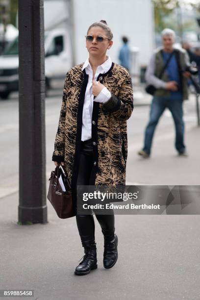 Guest wears a white shirt, a black and beige print coat, black leather pants, a burgundy bag, outside the Dries Van Noten show, during Paris Fashion...