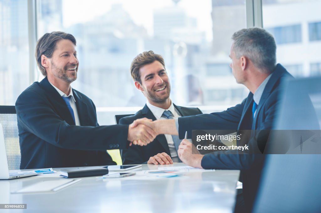 Businessmen shaking hands at the board room table.