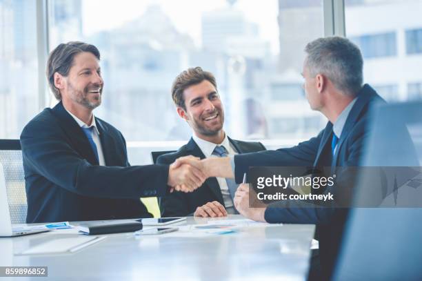 businessmen shaking hands at the board room table. - business agreement stock pictures, royalty-free photos & images