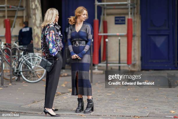 Guest wears a flower print top, black pants, a black bag, black shoes ; a guest wears a grey and blue V-neck long dress, a black belt, a studded...