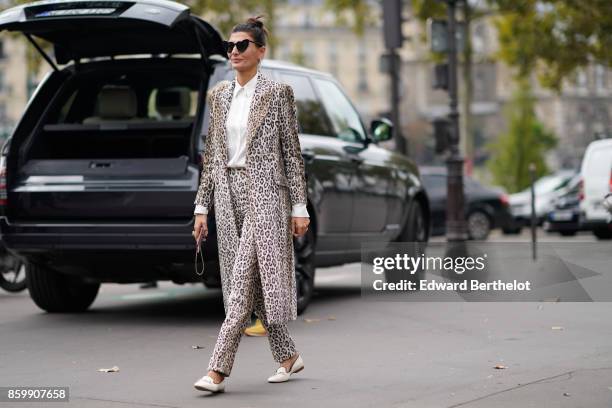 Giovanna Battaglia wears sunglasses, a white shirt, a leopard print coat, leopard print pants, white moccasins, outside the Dries Van Noten show,...