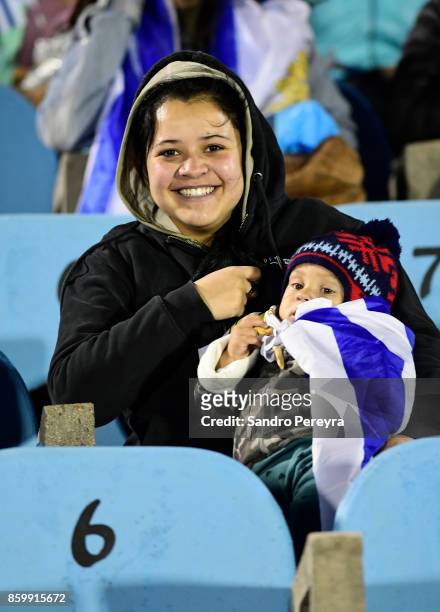 Fan of Uruguay holding a baby smiles prior a match between Uruguay and Bolivia as part of FIFA 2018 World Cup Qualifiers at Centenario Stadium on...