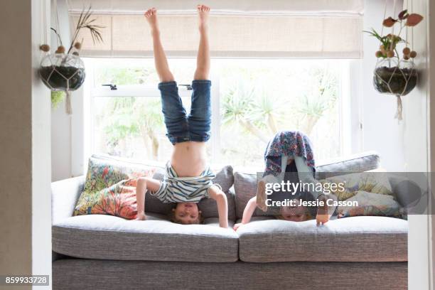 siblings playing on sofa doing headstands - al revés posición descriptiva fotografías e imágenes de stock