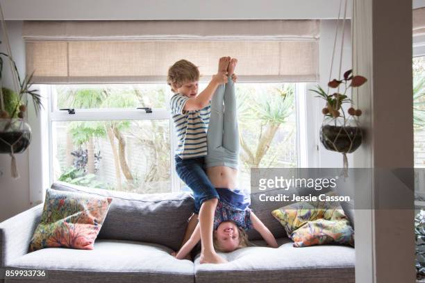 Siblings - brother helping and supporting sister to do a headstand