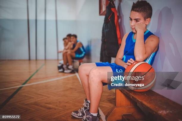 sad boy not playing basketball and sitting on the bench - basketball bench stock pictures, royalty-free photos & images