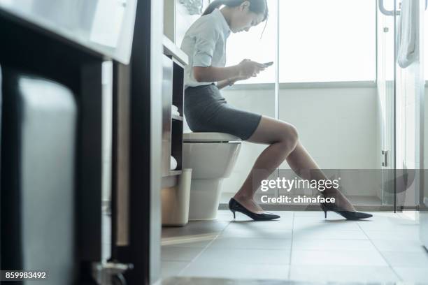 woman sitting on flush toilet typing smartphone - woman toilet stock pictures, royalty-free photos & images