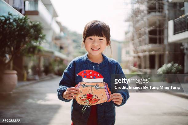 lovely little girl holding a diy funny paper santa claus mask smiling at the camera joyfully. - child christmas costume stock pictures, royalty-free photos & images