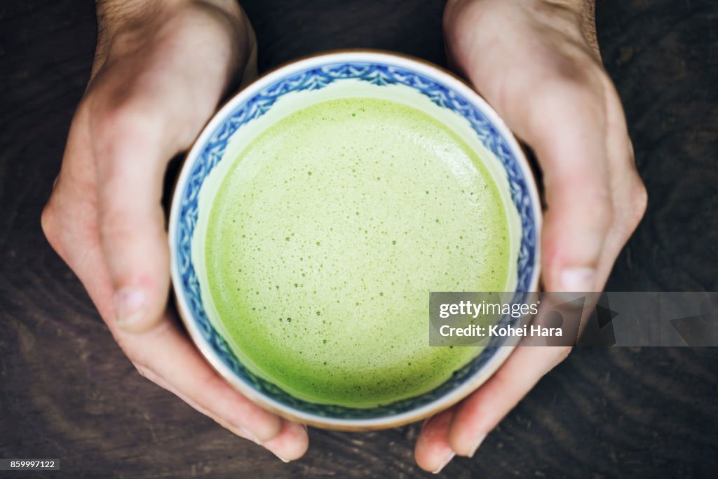 Hands of man holding a cup of Japanese powdered green tea