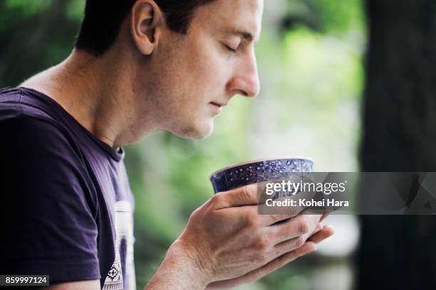 caucasian man enjoying japanese powdered green tea in the japanese garden - purple tee shirt stock-fotos und bilder