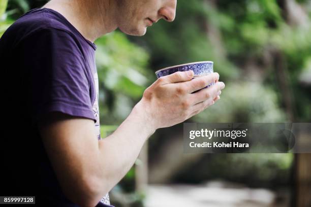 caucasian man enjoying japanese powdered green tea in the japanese garden - purple tee shirt stock-fotos und bilder