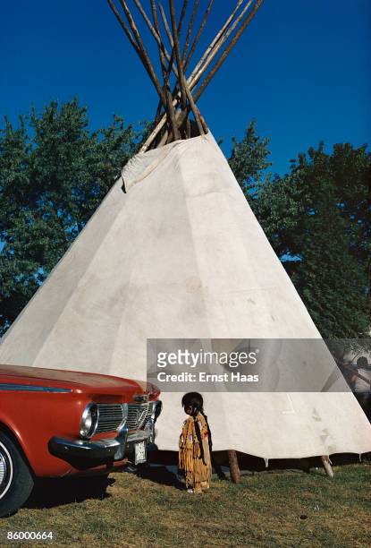 Little girl in Native American dress stands in front of a Plymouth Valiant and a teepee in Seattle, Washington State, 1975.