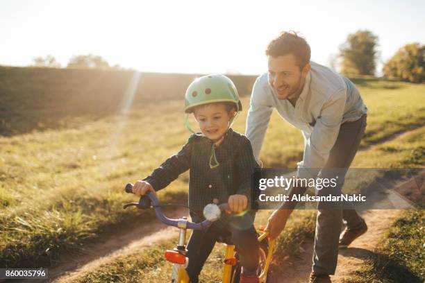 learning to ride a bicycle - father helping son wearing helmet stock pictures, royalty-free photos & images