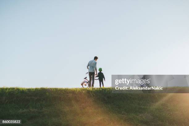 father and son on a bicycle lane - father helping son wearing helmet stock pictures, royalty-free photos & images