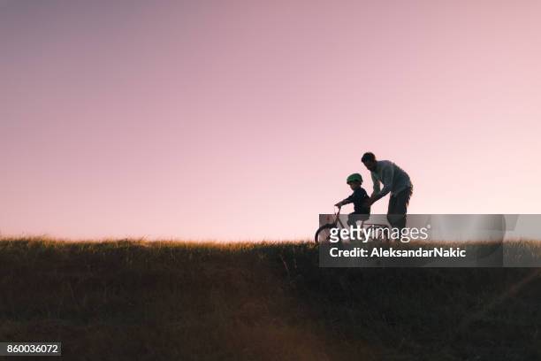 father and son on a bicycle lane - father helping son wearing helmet stock pictures, royalty-free photos & images