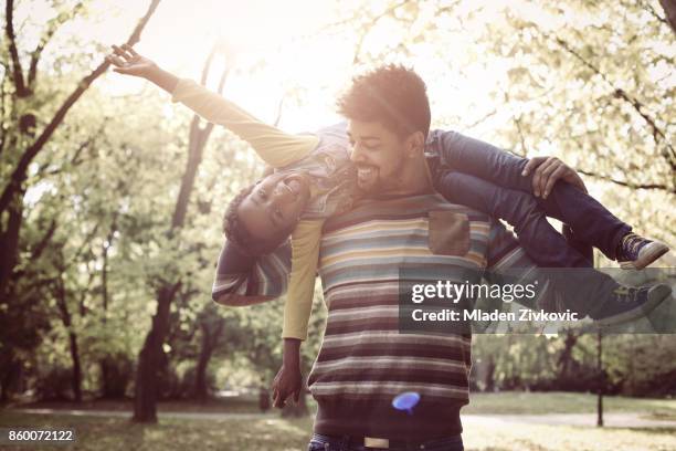 African American father with daughter on meadow. Girl lying on father shoulders.