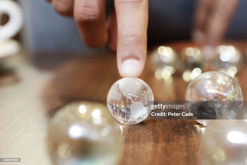 Finger resting on glass globe among other marbles