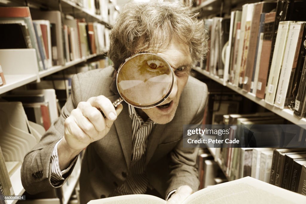 Crazy man looking in book with magnifying glass