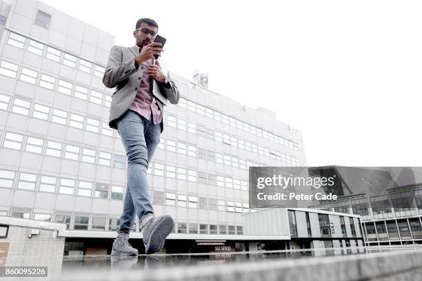 man walking in city looking at mobile phone - focus on background stock-fotos und bilder