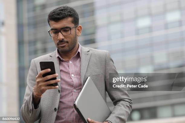 man walking in city looking at mobile phone - arab phone stock-fotos und bilder