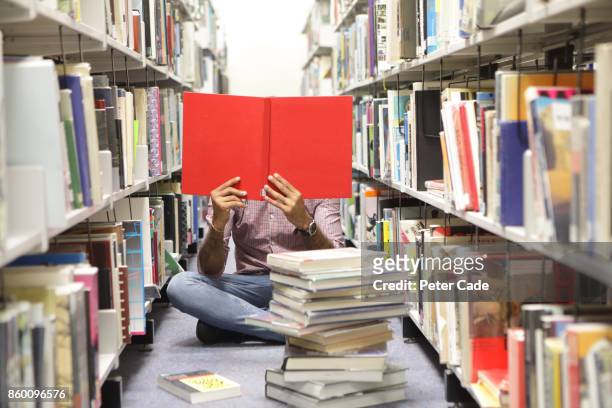 man sat on floor in library reading red book - stack of books stock pictures, royalty-free photos & images