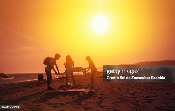 father and daughters fitting a towel on the beach on a radiant sunny day. - barcelona free stock-fotos und bilder