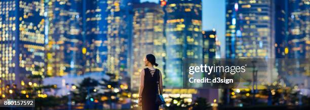 young businesswoman standing against illuminated cityscape of hong kong metropolitan at night - night before stock pictures, royalty-free photos & images