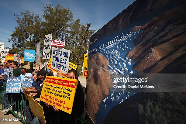 Marchers hold signs next to an aerial photograph of a lake with a low water level dated February 3, 2009 during a rally attended by California Gov....