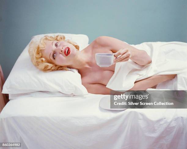 Portrait of Danish-born American model and actress Greta Thyssen as she lies, seemingly nude, in bed and holds a coffee cup, late 1940s or early...