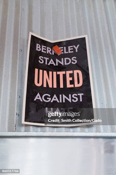 Inside a restaurant, workers have used a magnet to hang a poster reading "Berkeley Stands United Against Hate" on the metal hood of a stove, part of...