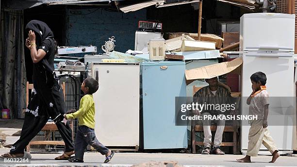 Woman and her children walk past a shopkeeper taking a nap as he waits for customers for used refrigerators and other household items in New Delhi on...